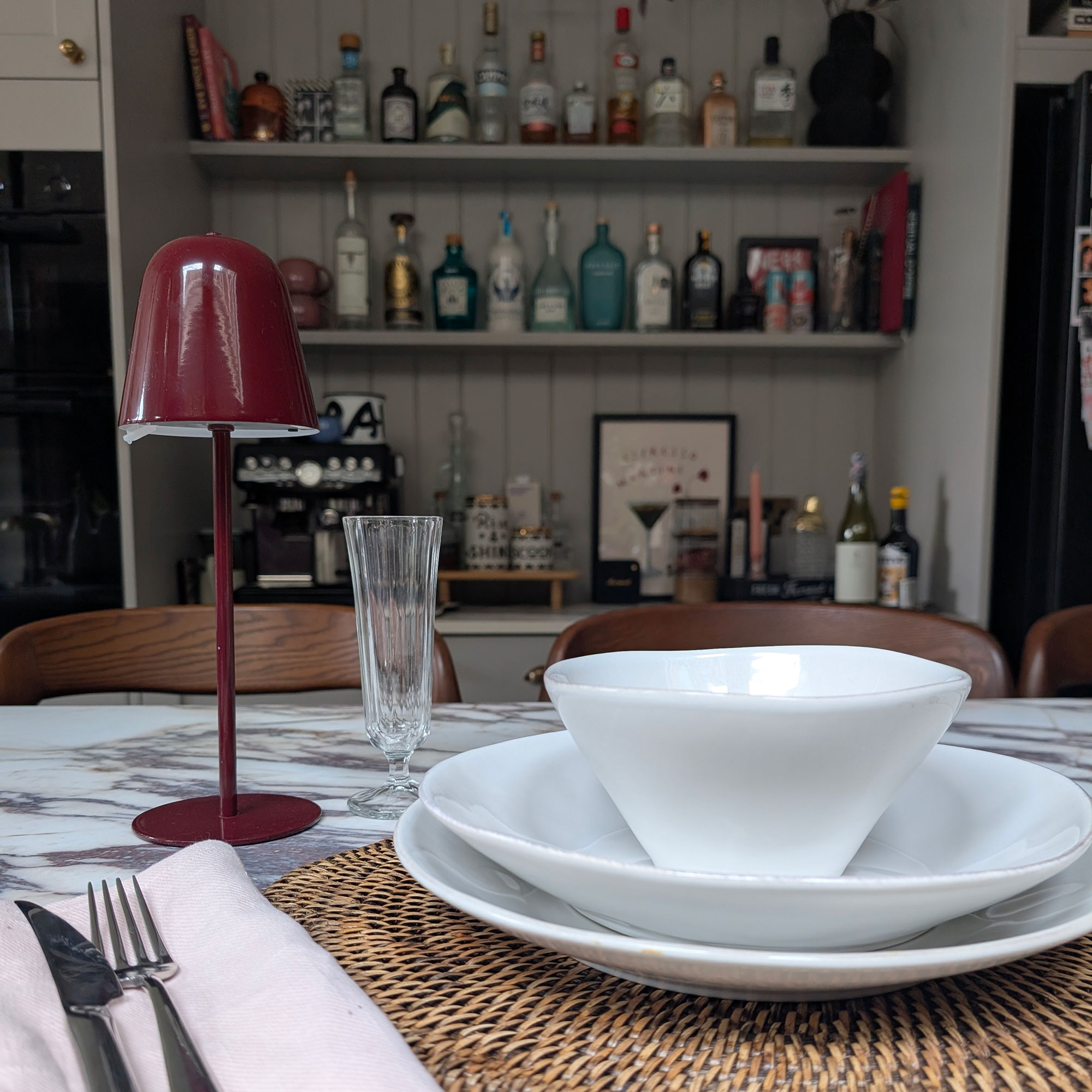 Table setting of white bowls and plated on woven placemat with red wireless light beside