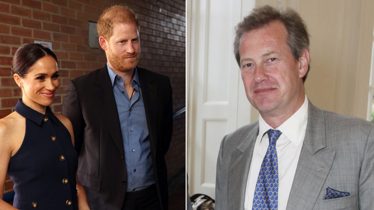 Meghan Markle wears a navy dress and Prince Harry wears a blue shirt with a dark suit, and Lord Ivar Mountbatten smiles while wearing a gray suit