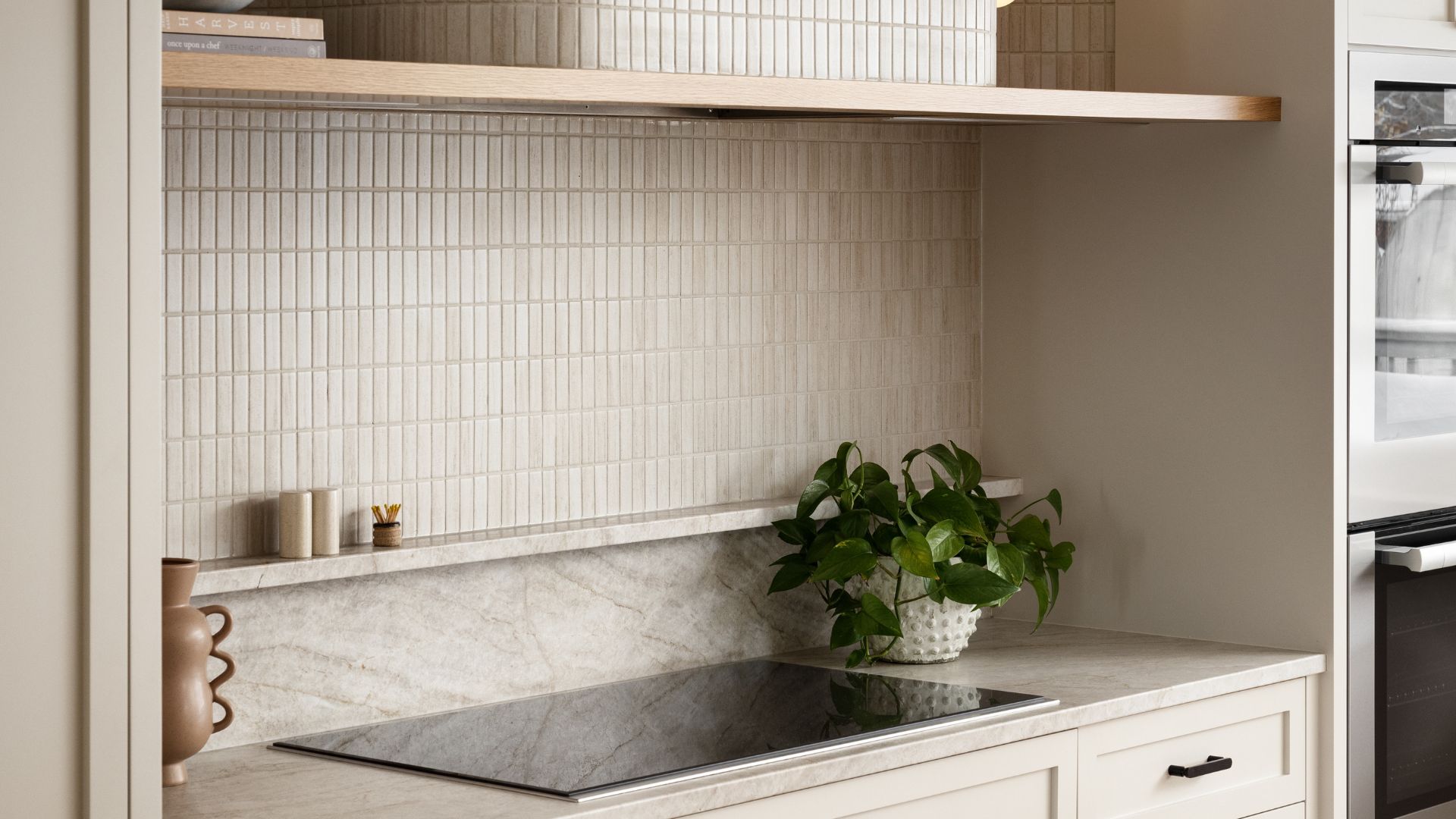 A minimalist kitchen with a tile backsplash, a stone counter and an induction hob. A structured vase and a potted houseplant are also on display.