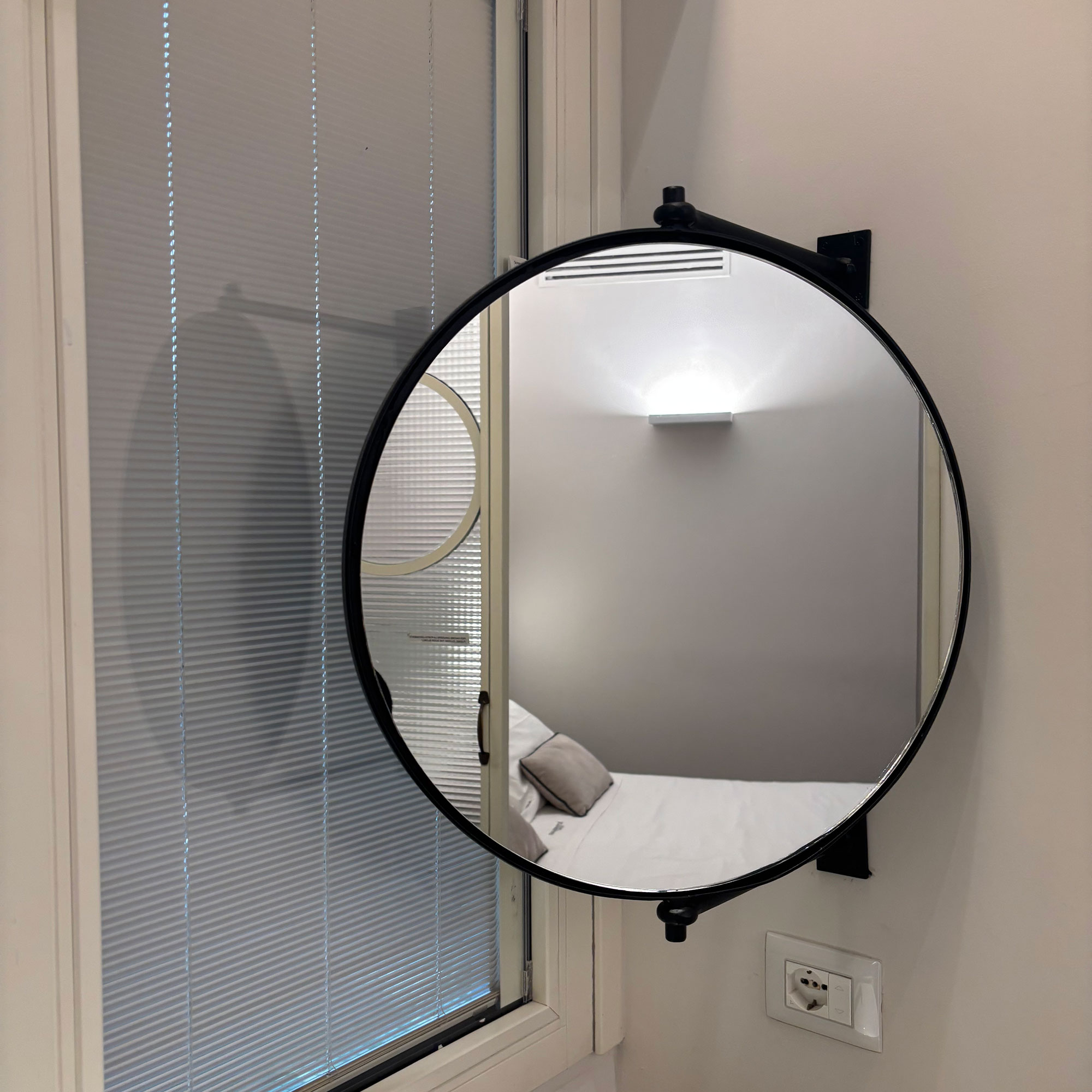 Rounded mirror in bathroom showing bed in reflection