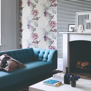 A living room with a striped and floral wallpaper with pieces of the wallpaper framed and placed on the fireplace mantel