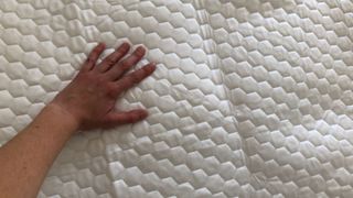 A hand feels the Brooklyn Bedding Luxury Cooling Mattress Protector to test its temperature control