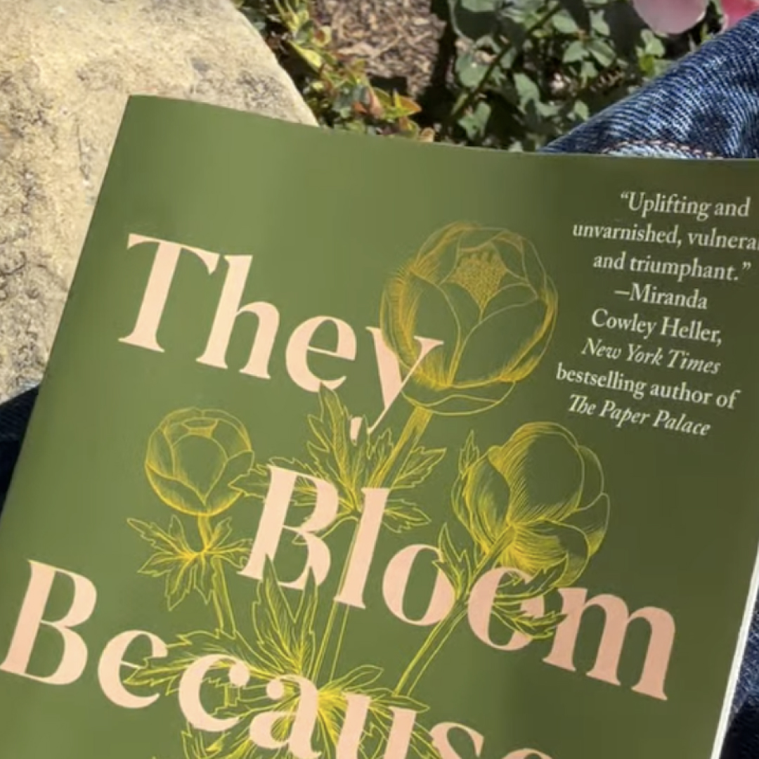 Meghan Markle holding a green book titled They Bloom Because of You 