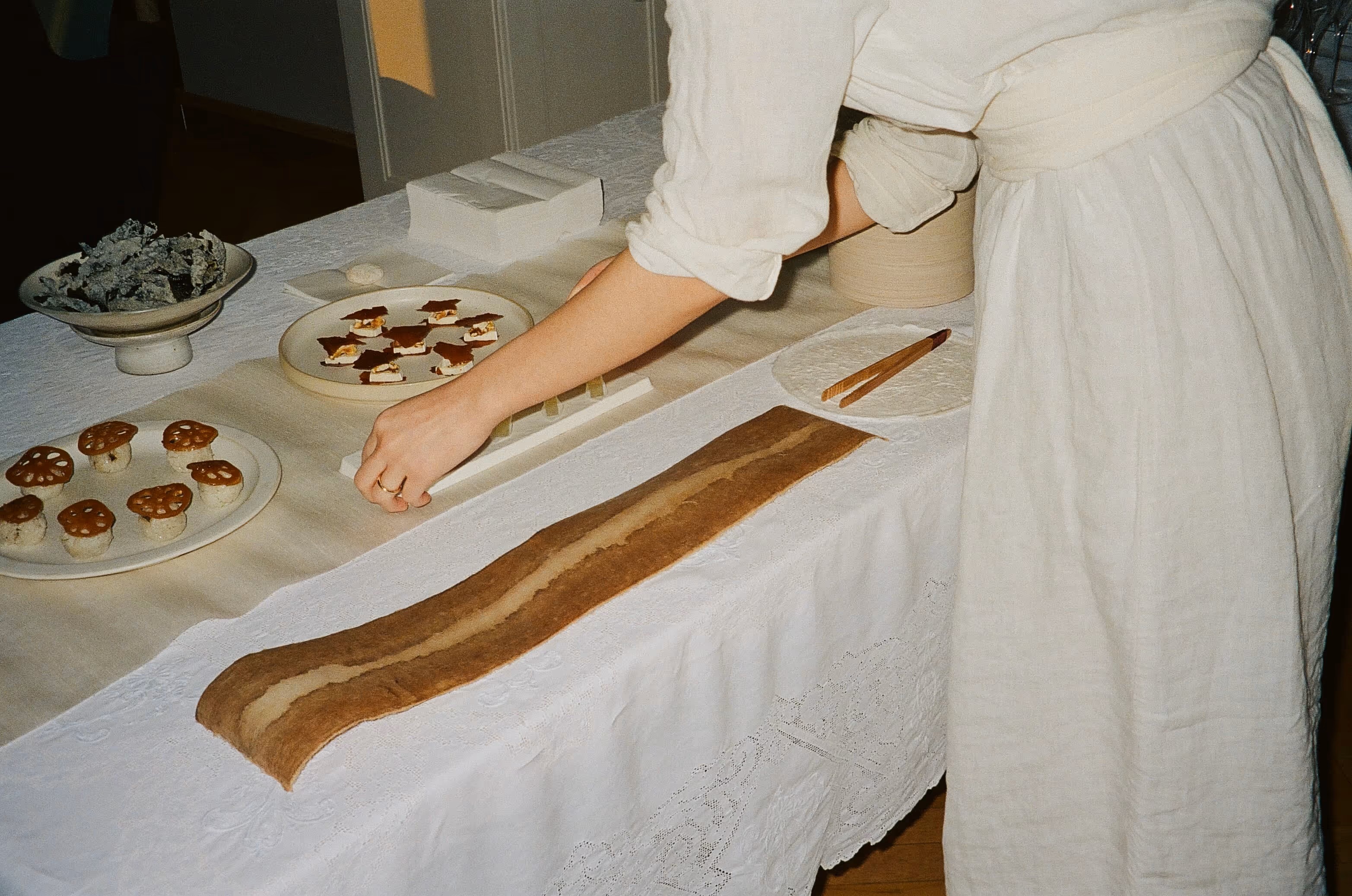 A woman dressed in white linen clothing preps a tablescape filled with sculptural, edible installations.