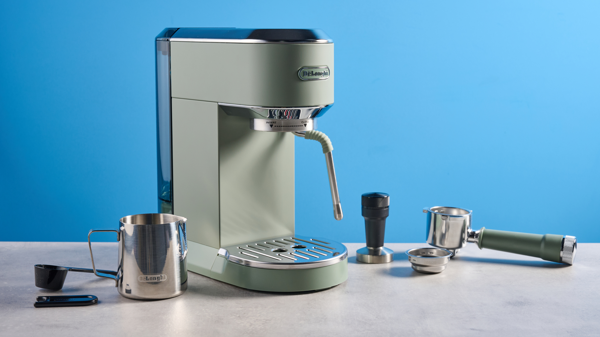 DeLonghi Dedica Duo in the green colorway with accessories photographed on a blue background. 