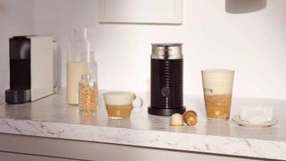 The Nespresso milk frother on a countertop with milk and a range of coffee types