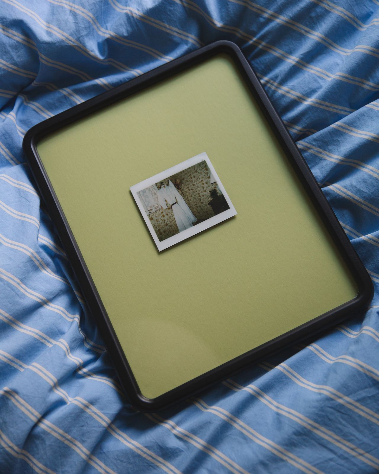 Image of a black picture frame with green mat boarding laying on a blue and white stripped bedding.