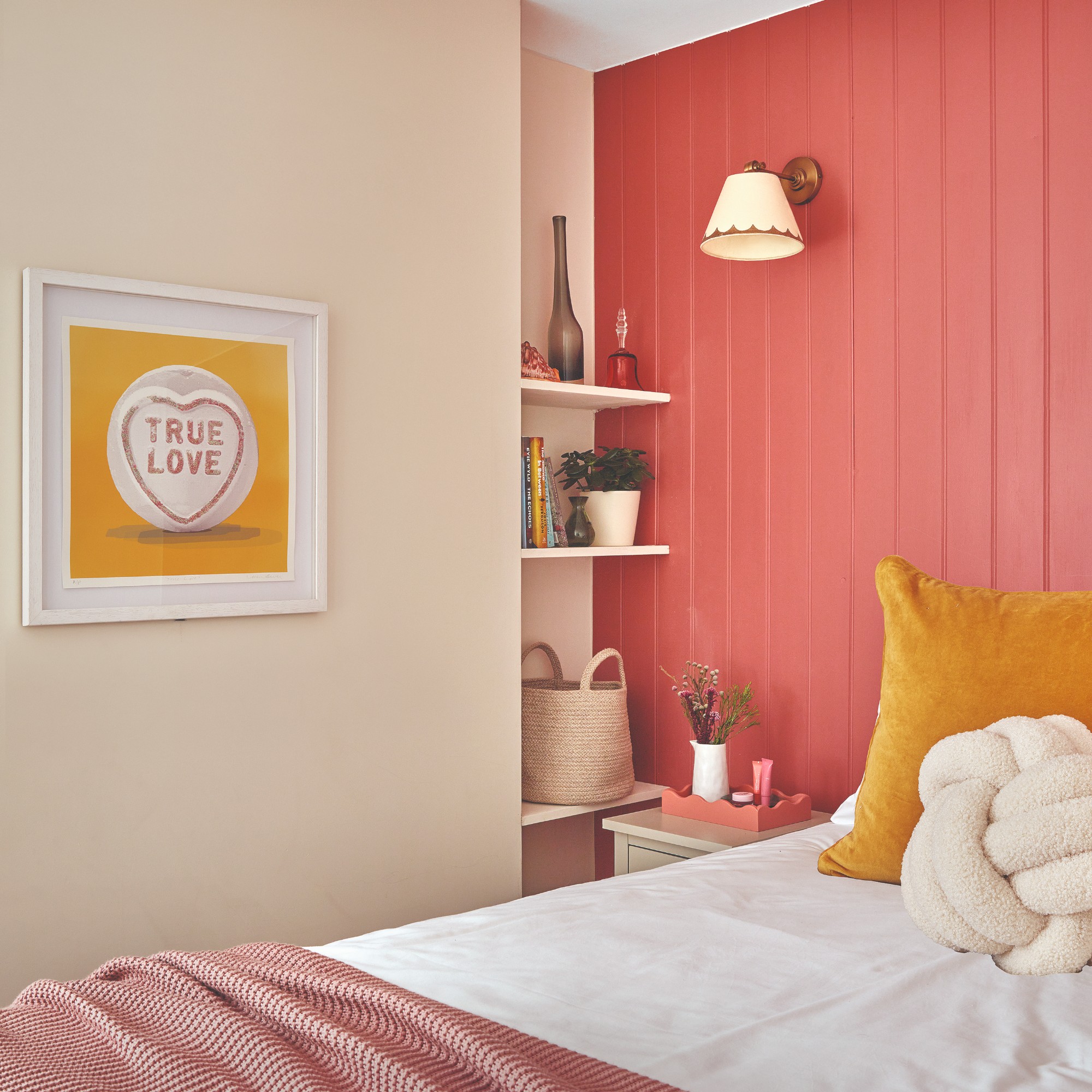 A bedroom with a blush-toned wall and a coral pink panelled feature wall