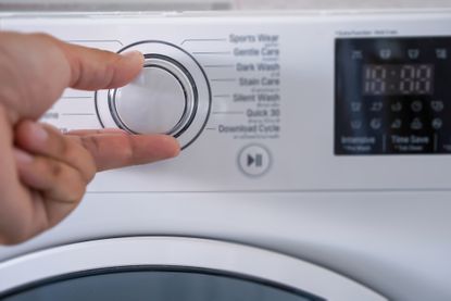 Cropped Hand Of Person Adjusting Washing Machine dial