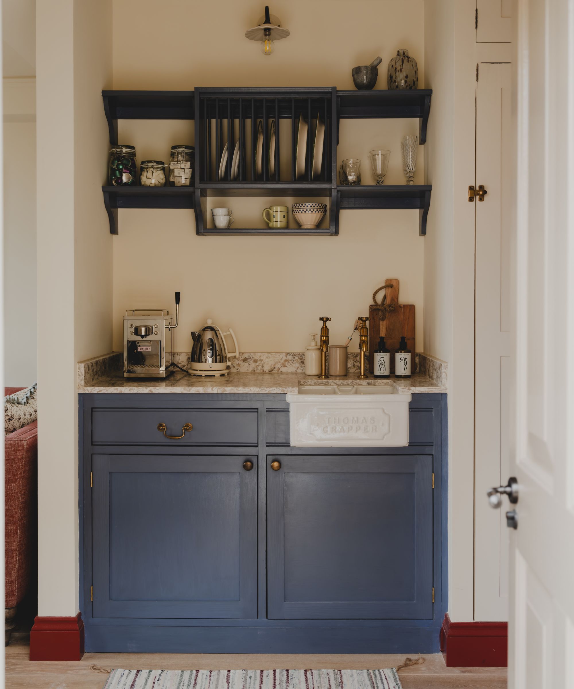 a tiny two cabinet size kitchenette in the cotswolds with blue painted lower cupboards, a Thomas Crapper sink, and open shelving above