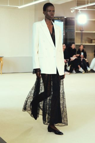Altuzarra model wearing a white blazer with a lace skirt underneath.