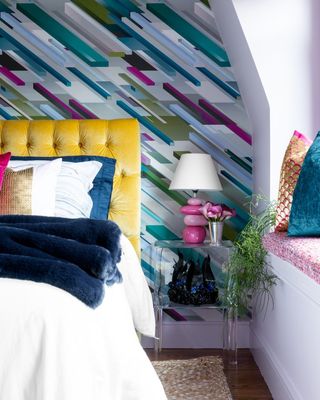 Colorful modern bedroom with bold rainbow colored wallpaper and yellow headboard