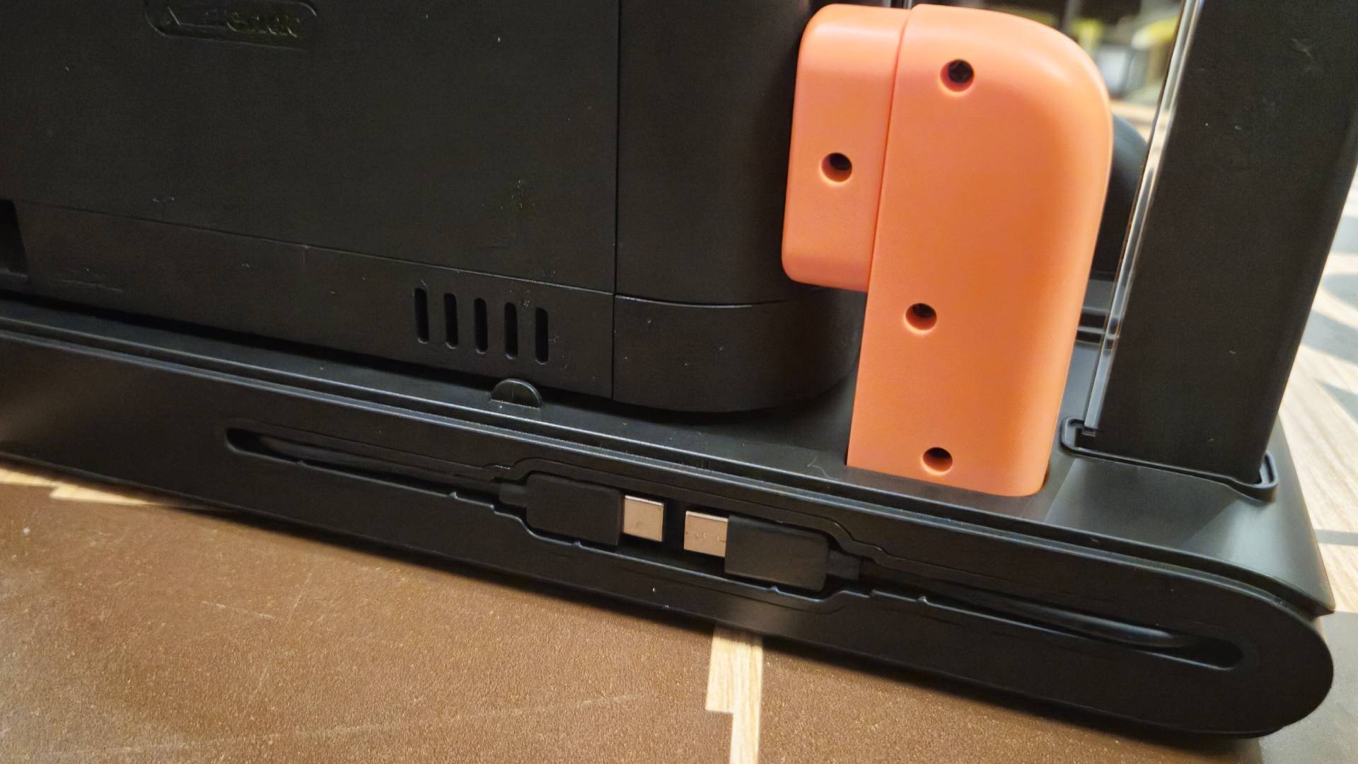 Photo of the back of a charging stand, showing a red adapter plugged into the side of a Switch 2 dock.
