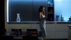 Philips Hue Lightstrip deals 2023, image shows woman in room with blue uplighting on the shelves behind her