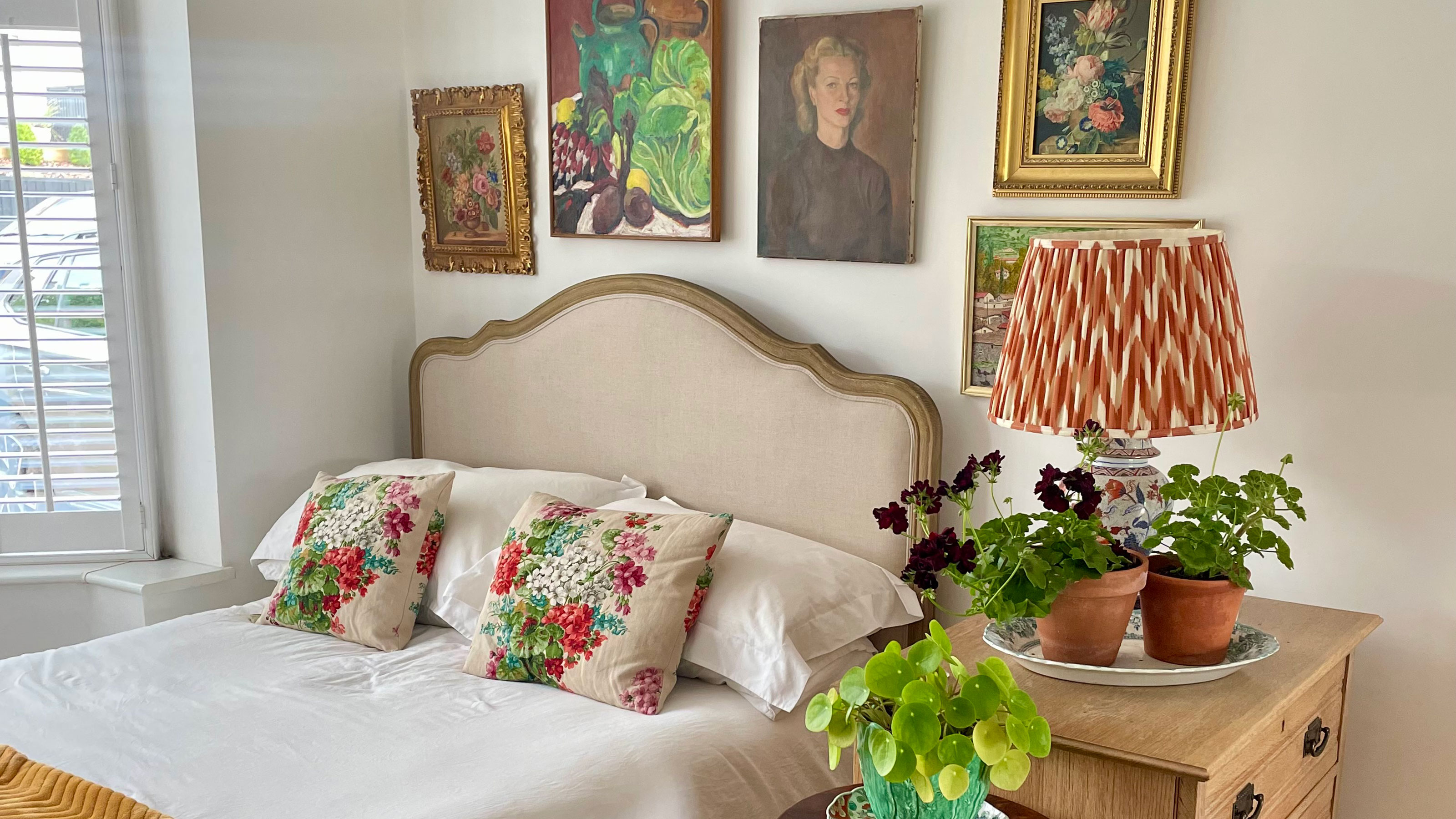 Gallery wall above bed, with bedside table holding table lamp and houseplants