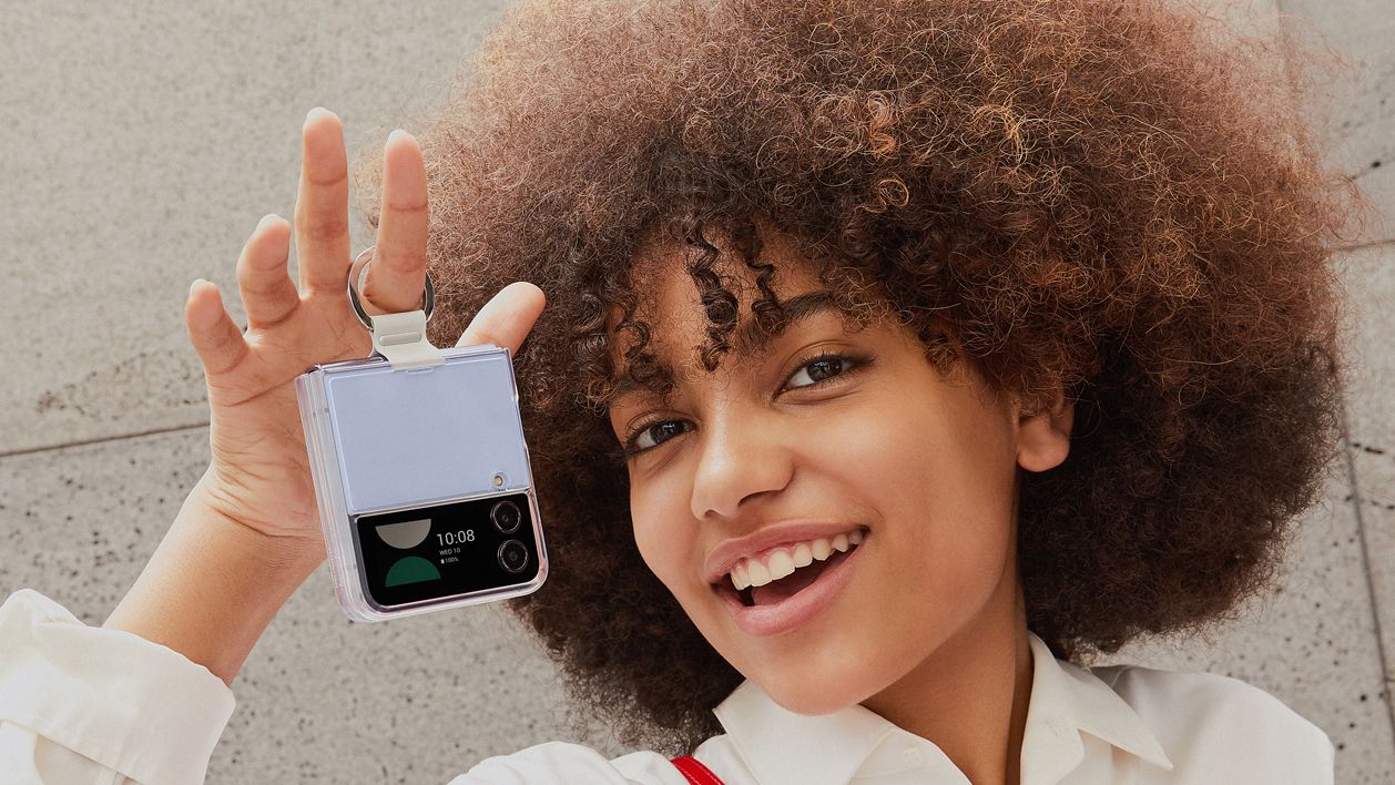 Samsung Galaxy Z Flip 4 foldable phone being held by woman with brown curly hair and white shirt