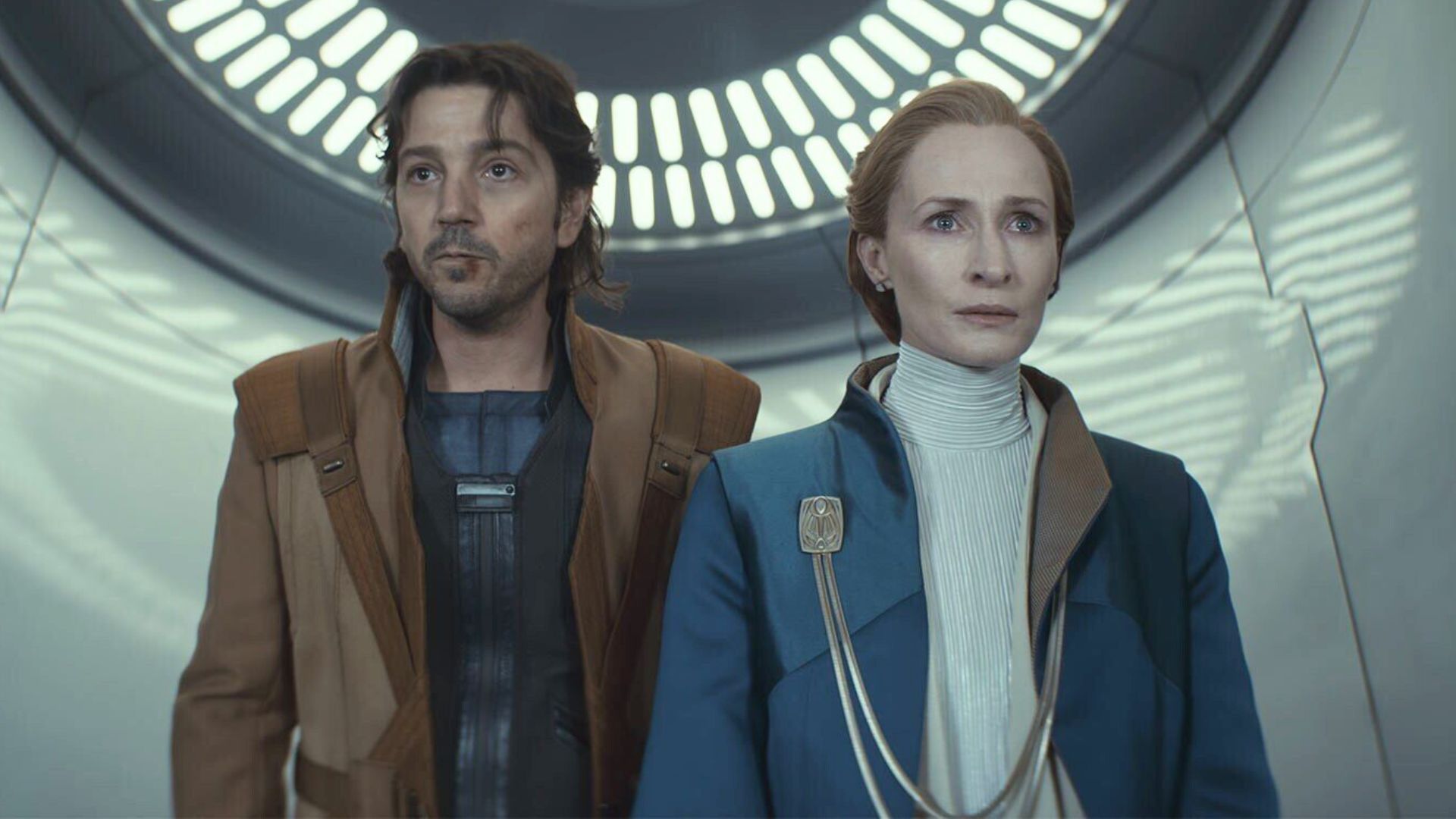 Diego Luna and Genevieve O&#039;Reilly stand next to each other looking at something offscreen