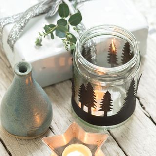 Glass jar tea light holder on wooden table with a wrapped gift and star candle holder