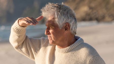 Senior man at the beach shielding his eyes from the sun 