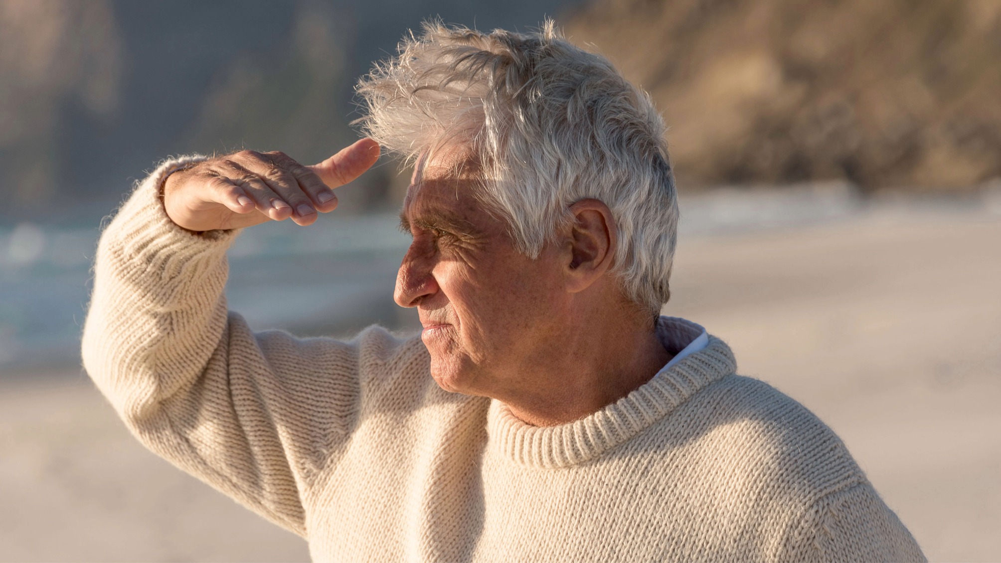Senior man at the beach shielding his eyes from the sun 
