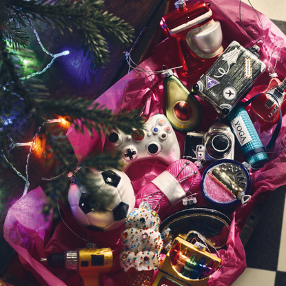 Box with pink tissue paper holding M&S's hobby-themed baubles. There is a stand mixer, avocado, camera, football, drill and yoga mat