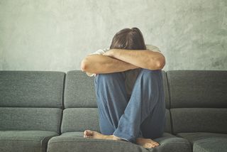 A man sits on a couch, crying and hiding his face