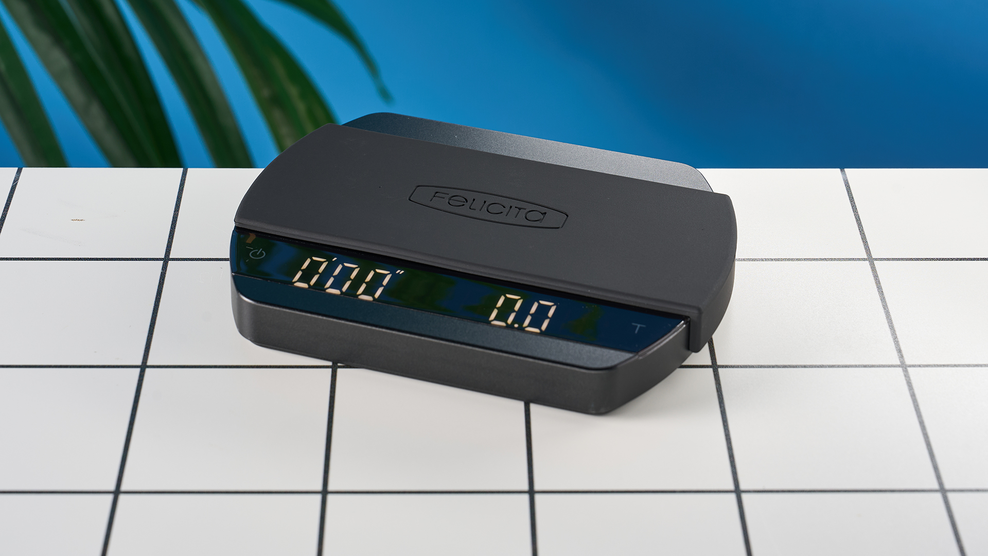 a luxury coffee scale made by Felicita Arc is photographed against a blue background with its weight, USB-C cable and silicone mat