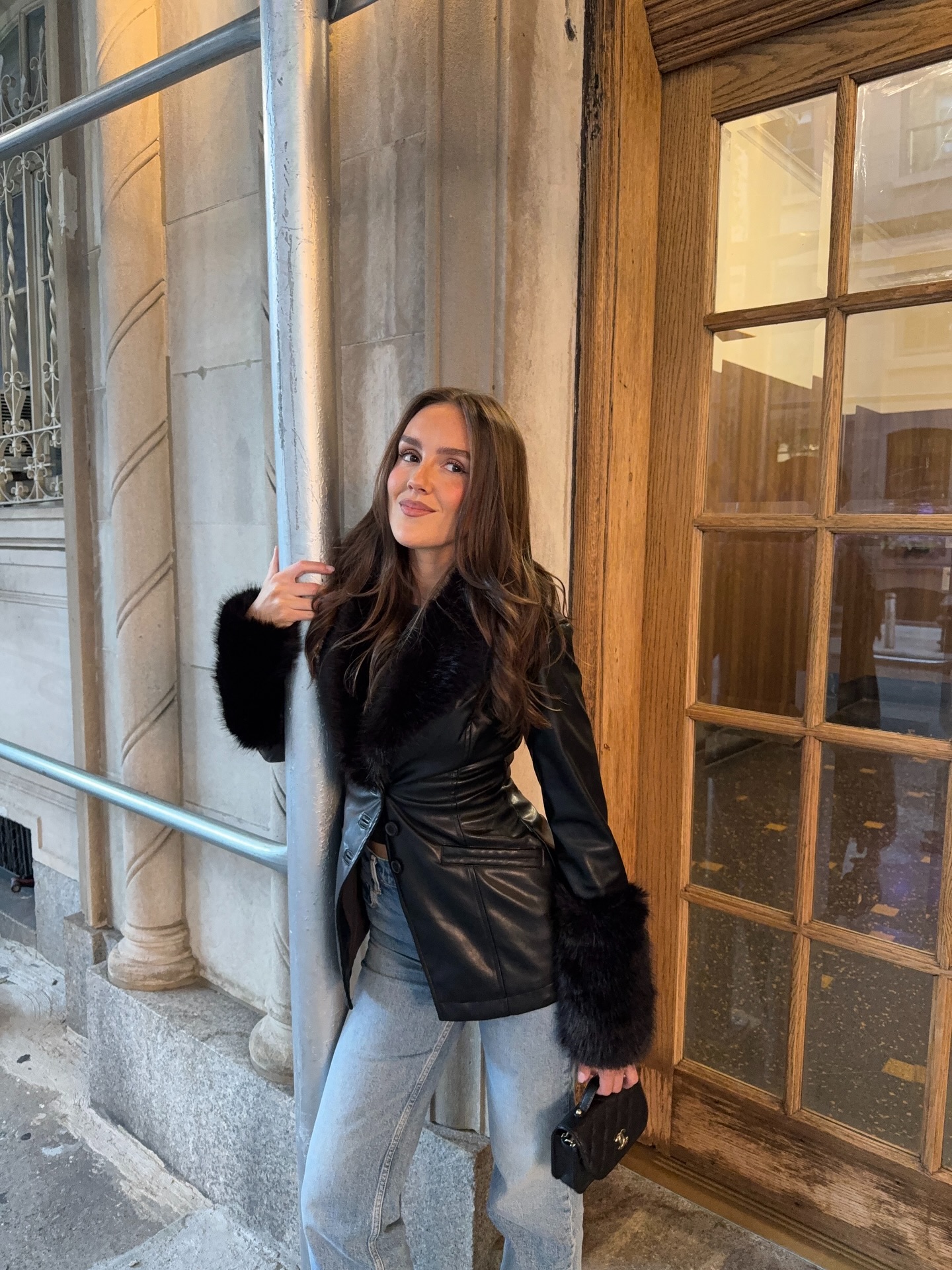 An image of @emmaleger wearing a fur-trim leather jacket and blue jeans, an example of what to wear to a cocktail bar.