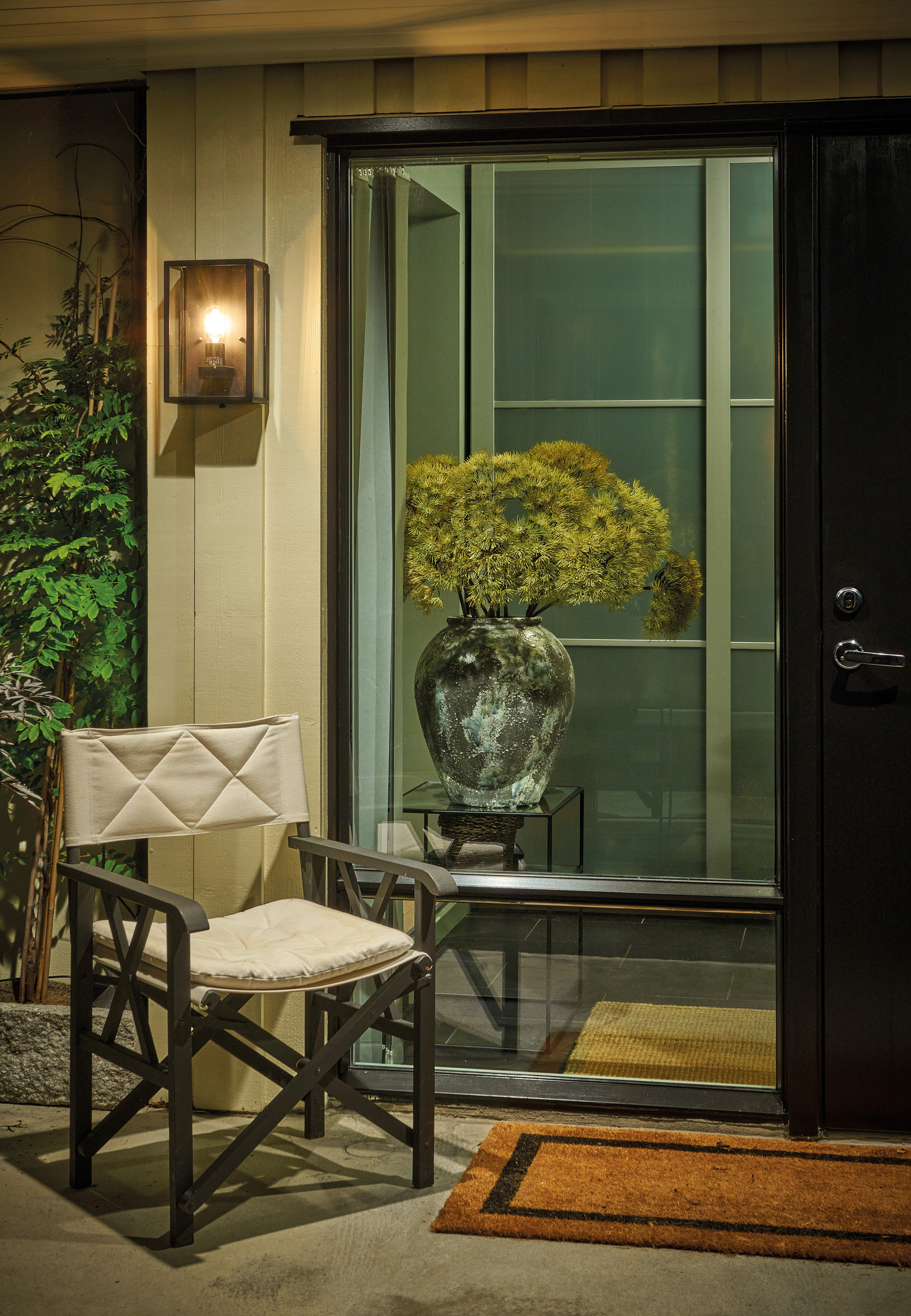 A front porch with a chair, a doormat, and a modern porch light on the wall