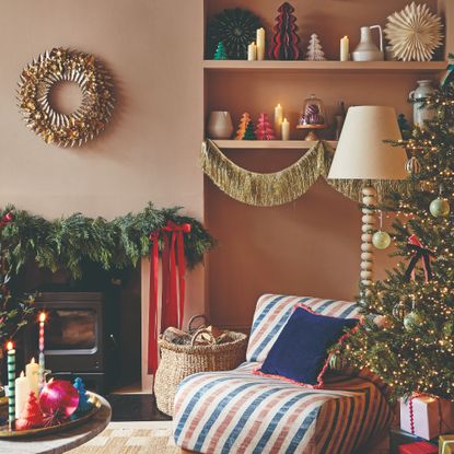 A living room decorated for Christmas with a lit-up Christmas tree, a gold tinsel garland decorating shelves and a foliage Christmas garland adorning the mantelpiece