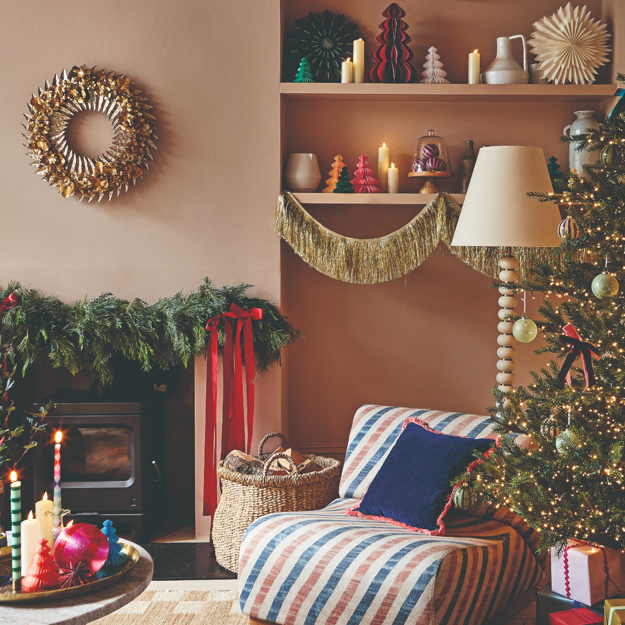 A living room decorated for Christmas with a lit-up Christmas tree, a gold tinsel garland decorating shelves and a foliage Christmas garland adorning the mantelpiece