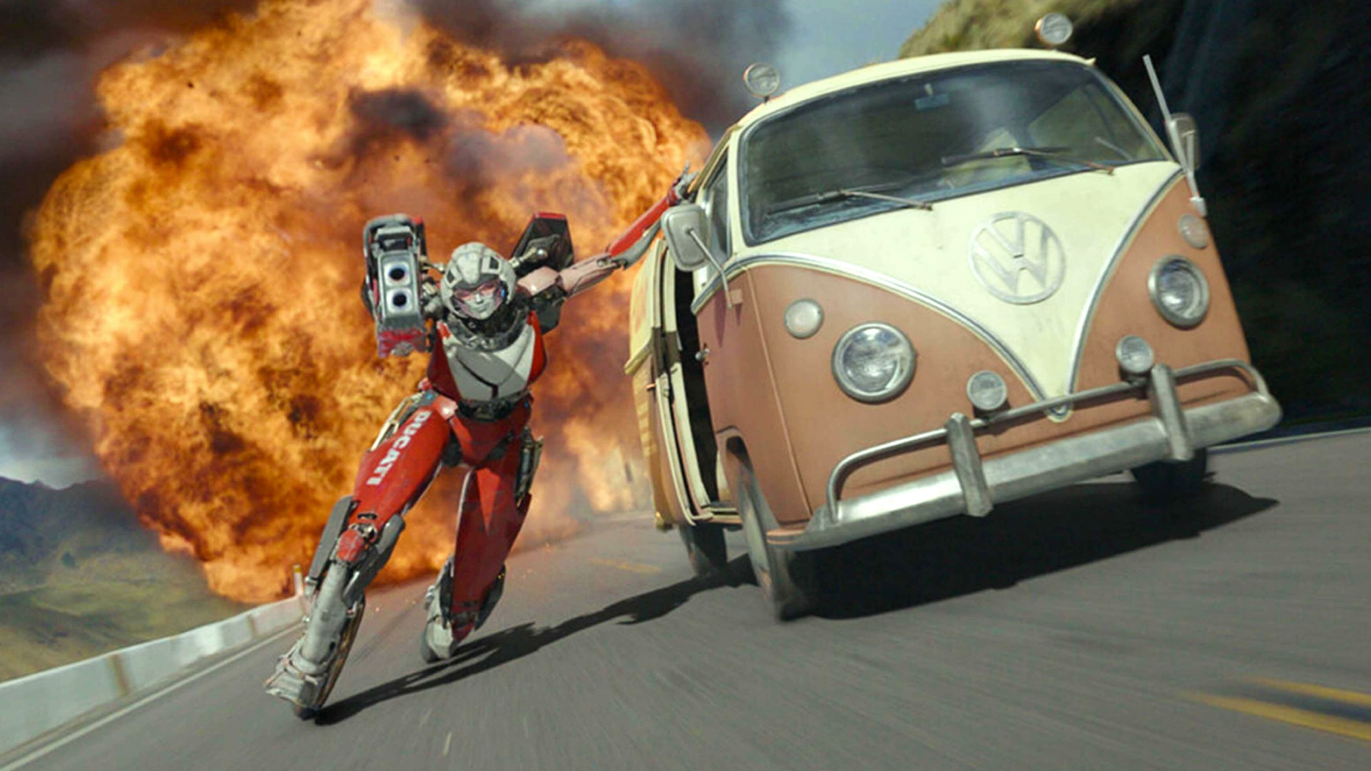 Arcee (voiced by Liza Koshy) holds onto a Volkswagen bus to outrun an explosion in Transformers: Rise of the Beasts