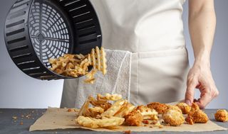 En man häller upp pommes frites som har tillagats i en airfryer på ett bakplåtspapper.