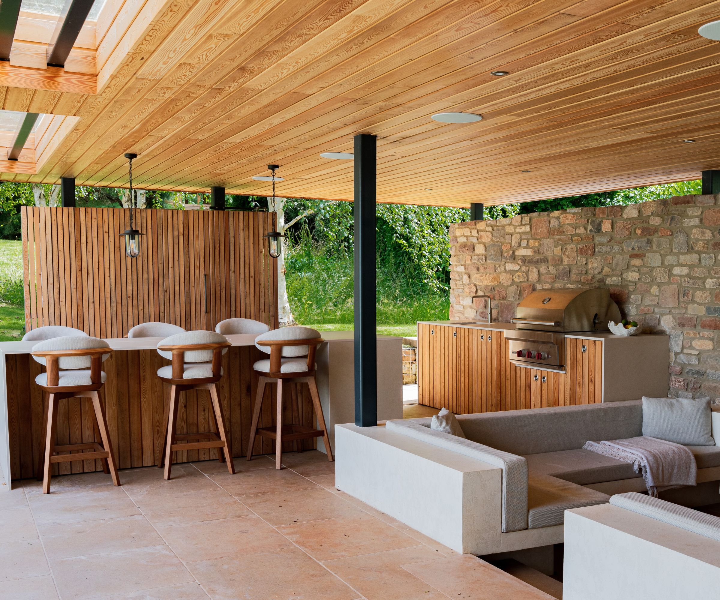An outdoor kitchen made from wood and limestone, surrounded by a dining space and living area