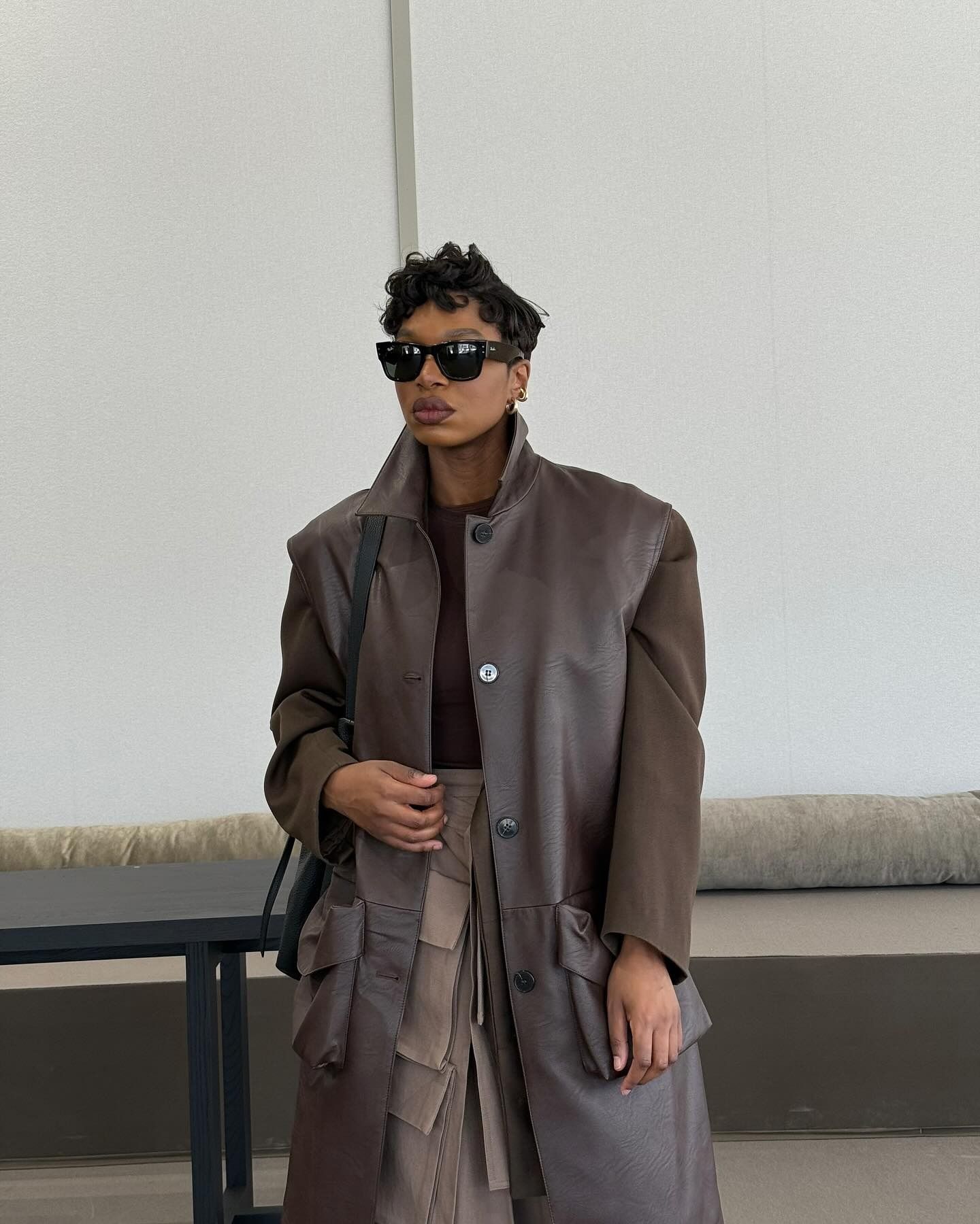 A woman standing in a brown coat with a curly pixie haircut