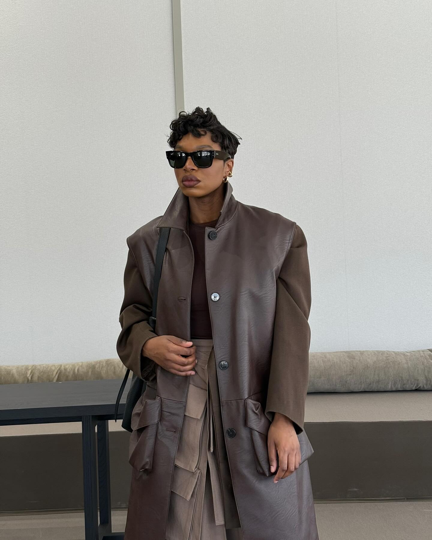 A woman standing in a brown coat with a curly pixie haircut