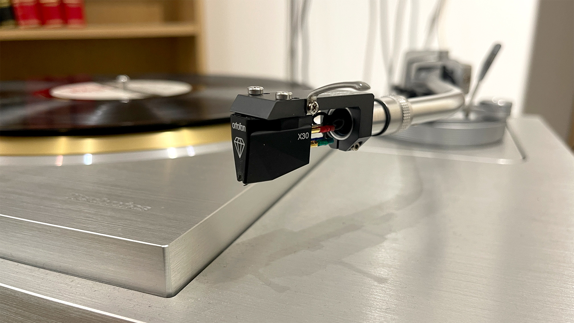 Ortofon MC X30 moving coil cartridge on tonearm not on record, record player with vinyl on platter in background