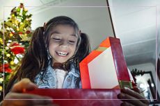 A young girl opening a present in front of a Christmas tree