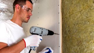 Man drilling in screws into plasterboard on insulated stud wall