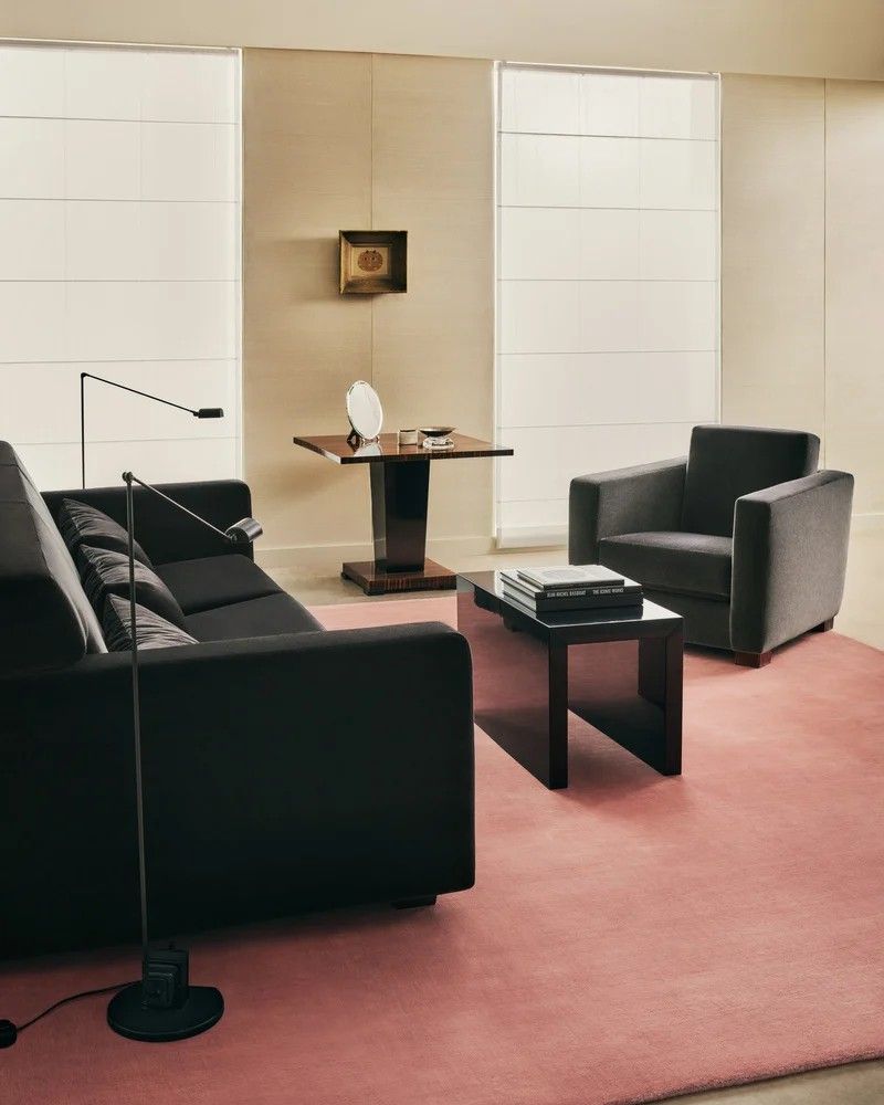 Image of a modern living room with white walls and a bubble gum pink rug and black furniture.