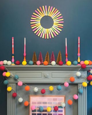 grey fireplace with colourful pom pom galrlands, candle sticks, a lolipop wreath and dark blue walls