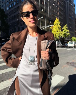 @leandramcohen wearing brown satin coat, white dress, and silver pendant necklace