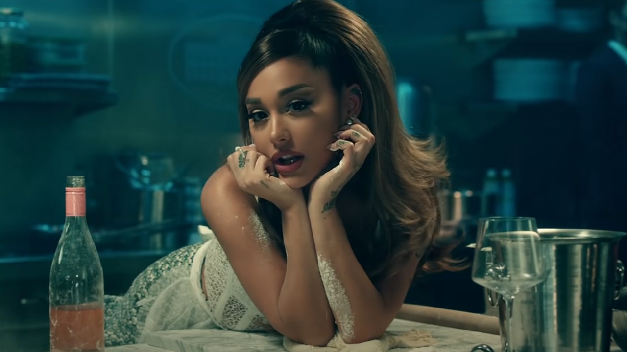 Ariana Grande leaning against her hand standing in a kitchen in the Positions music video