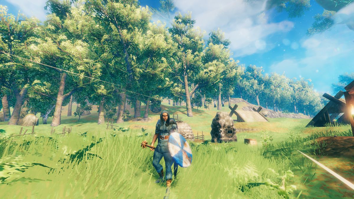 Valheim character stands with a bronze mace and wooden shield in the meadows. Two wooden huts are in the background and trees show in the distance