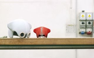 View of a light grey helmet next to a smaller red version pictured on a wooden surface