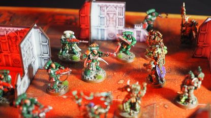 An array of Space Marine and Plague Marine models on an orange battlemat littered with MDF ruins