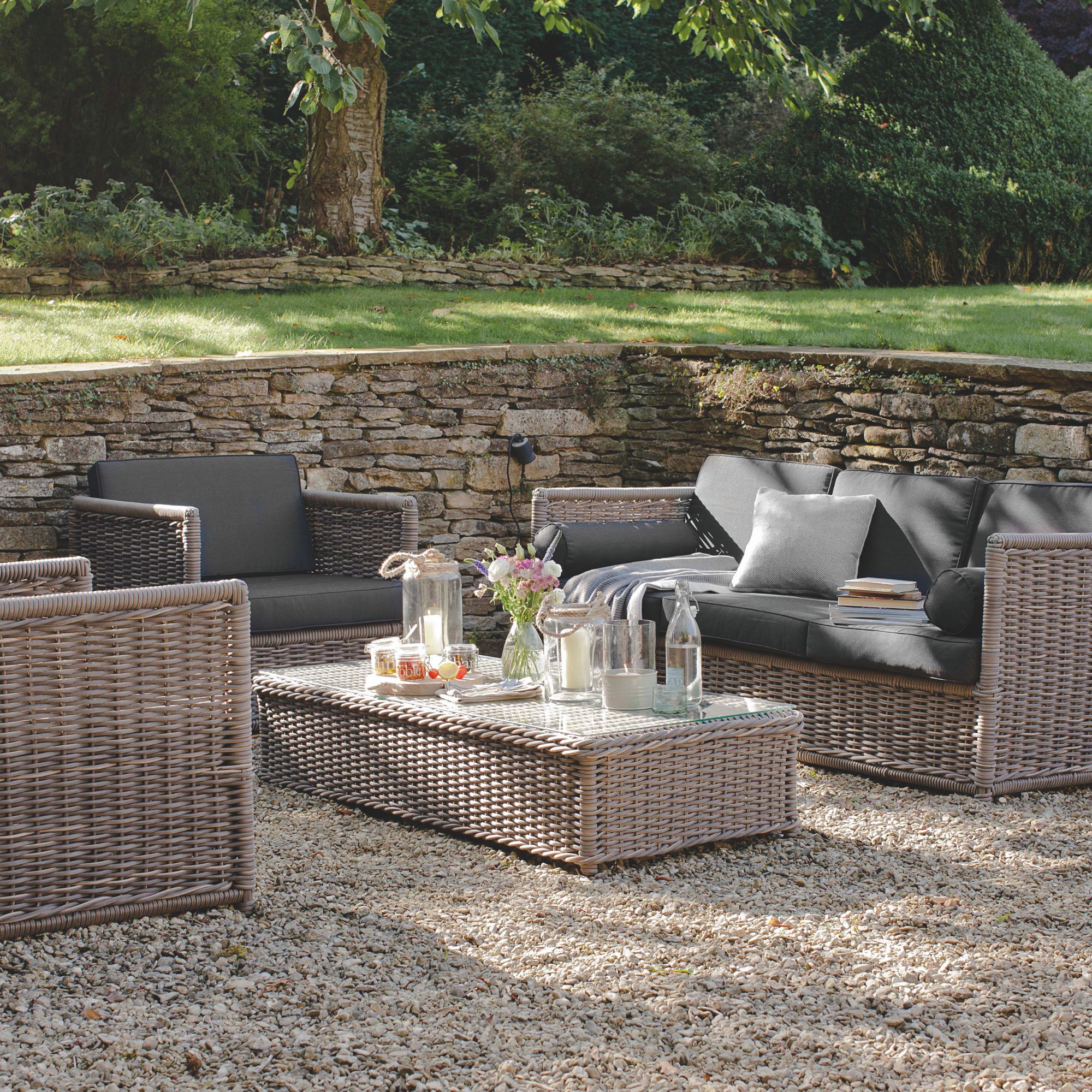 Grey rattan garden furniture including outdoor sofa, chairs and table on gravel patio area