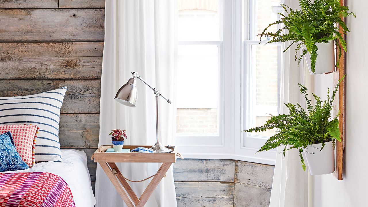 Wood panelled bedroom with sheer curtains, wooden bedside table and plants hanging from wall