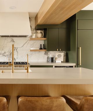 colors that go with dark green, kitchen with green cabinetry, marble backsplash, brass taps, white cooker hood, warm wood beam, stone countertops