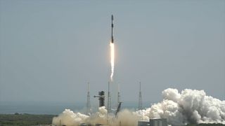 a white and black rocket lifts off into a daytime sky generating a bright flame and a white plume